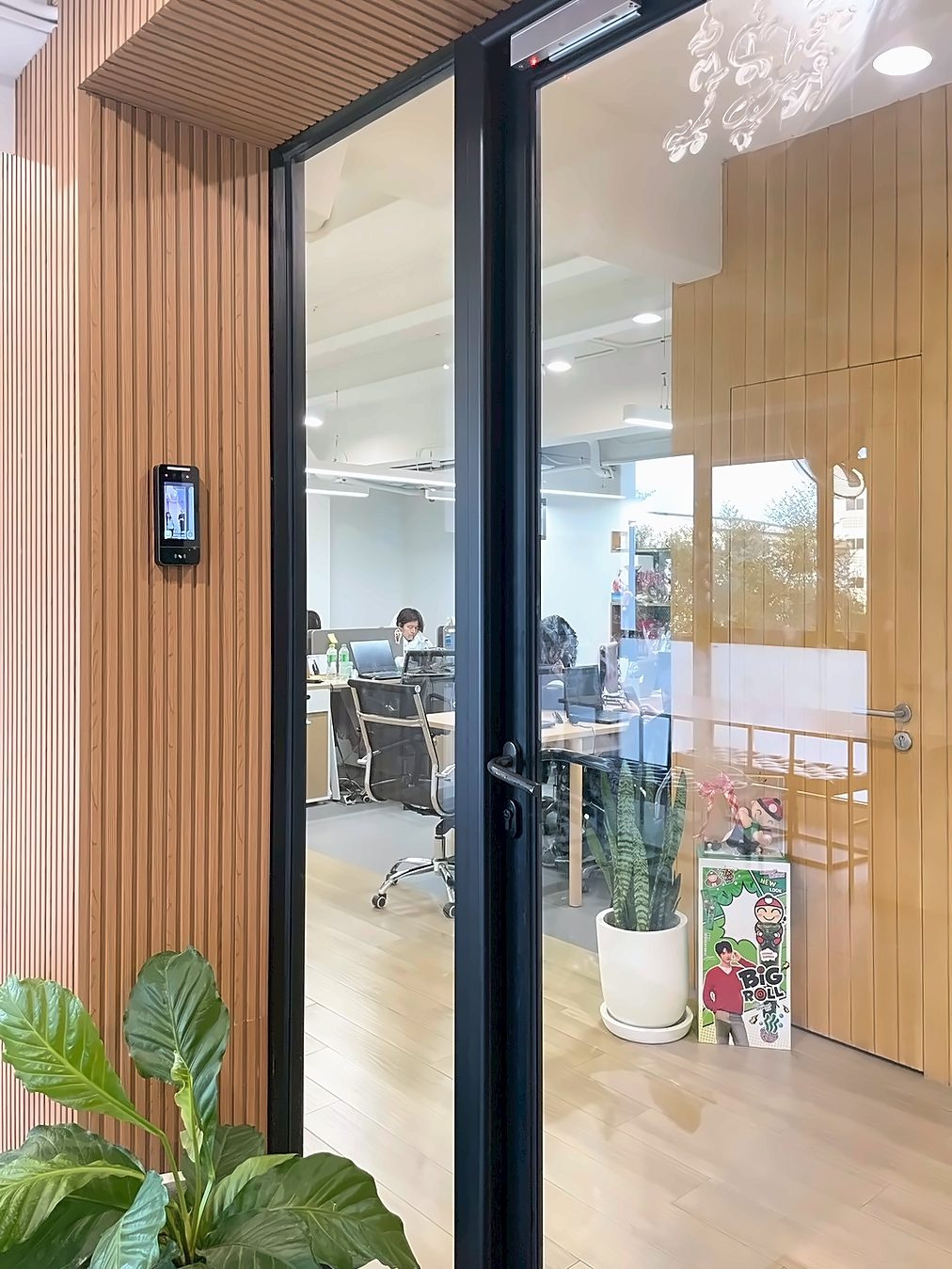 Glass entrance door of the Klick Digital Bangkok office, with wood-slat walls and the team working at their desks inside